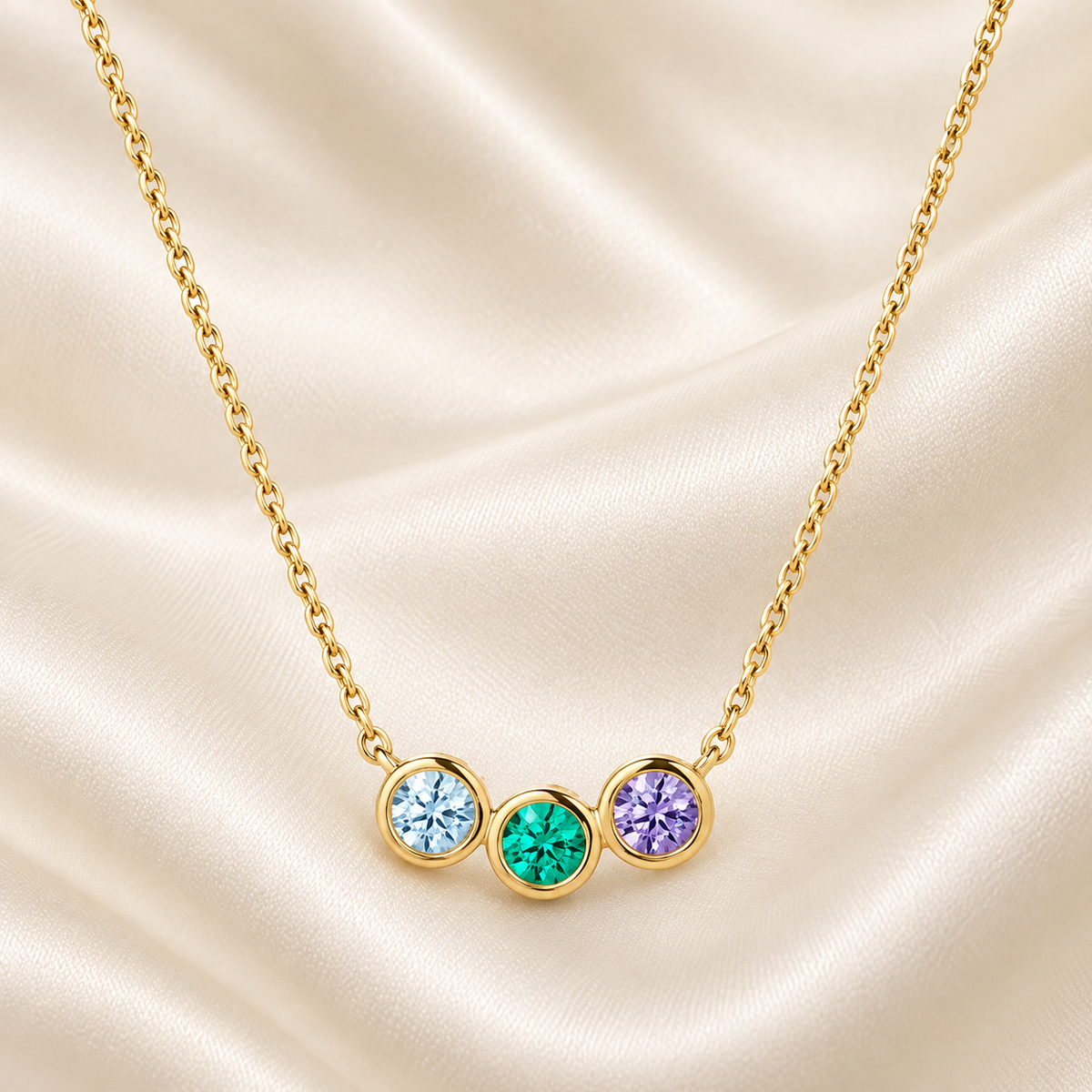 Three Stone Birthstone Necklace in gold on cream silk, close detail of the three bezel-set stones