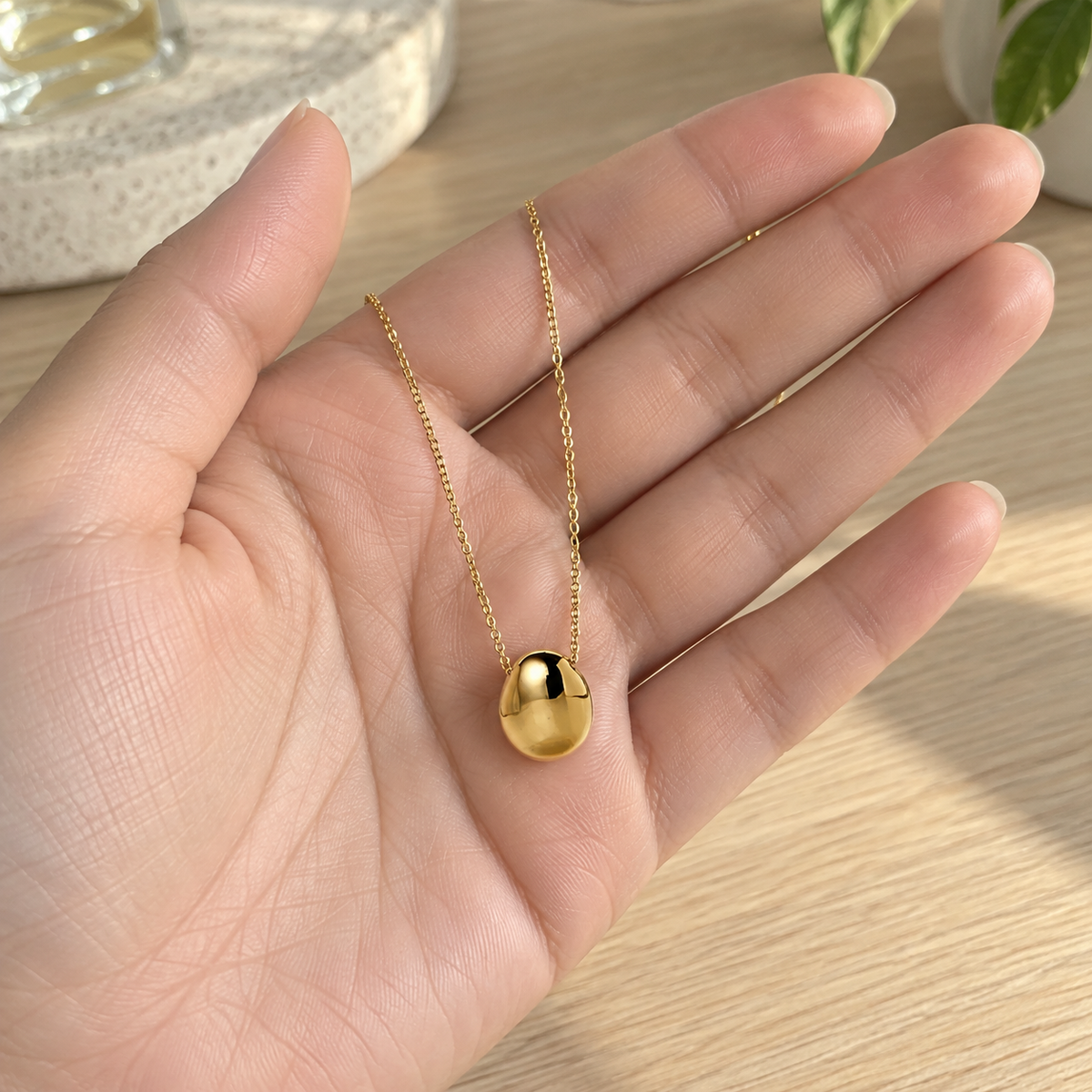 Gold Pebble Pendant Necklace held in an open hand for scale
